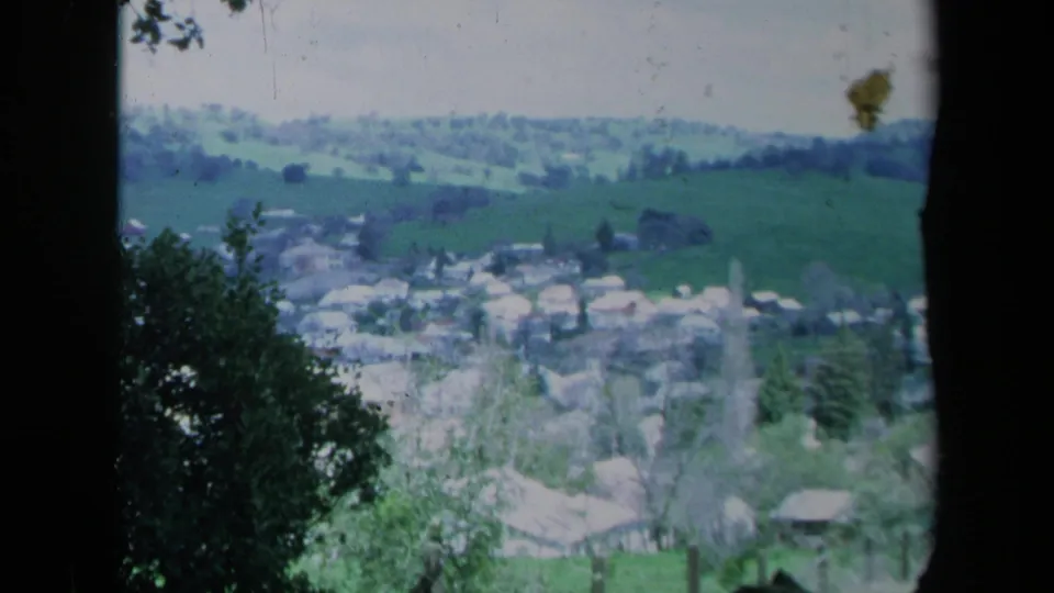 Faded-color 1969 California 8mm frame of a rural town and fields, framed by tree silhouettes and foreground vegetation.