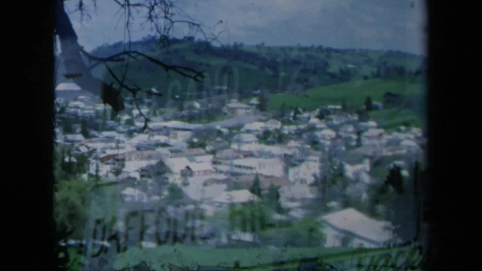 A similar 1969 California town overlook shows clustered houses below green hills, partially obscured by branches and dark frame edges.