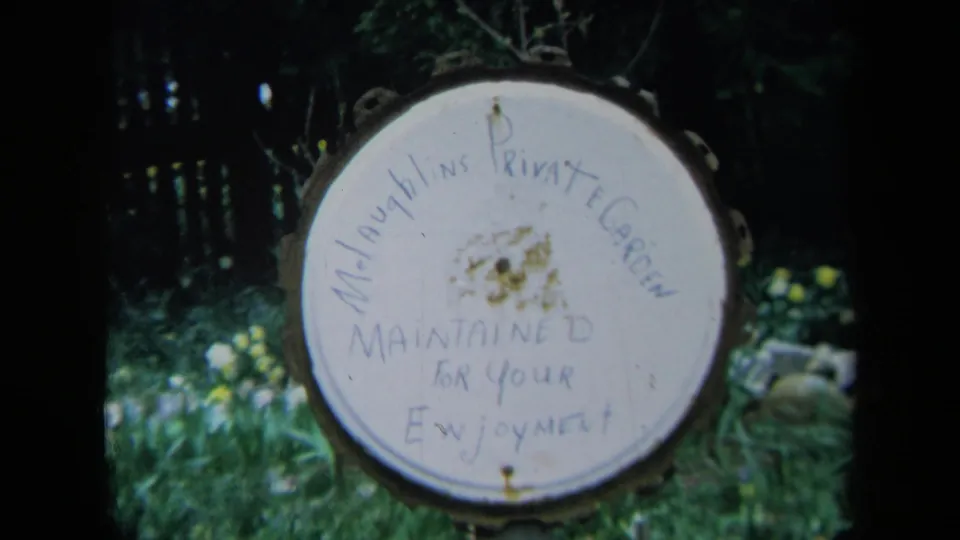 Close 1969 California home-movie view of a worn handwritten private garden sign surrounded by dark foliage.