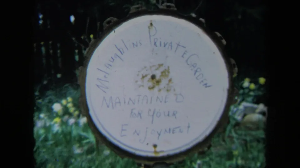 Final 1969 California frame of the private garden sign, with faded writing, yellow flowers, and leafy background visible.