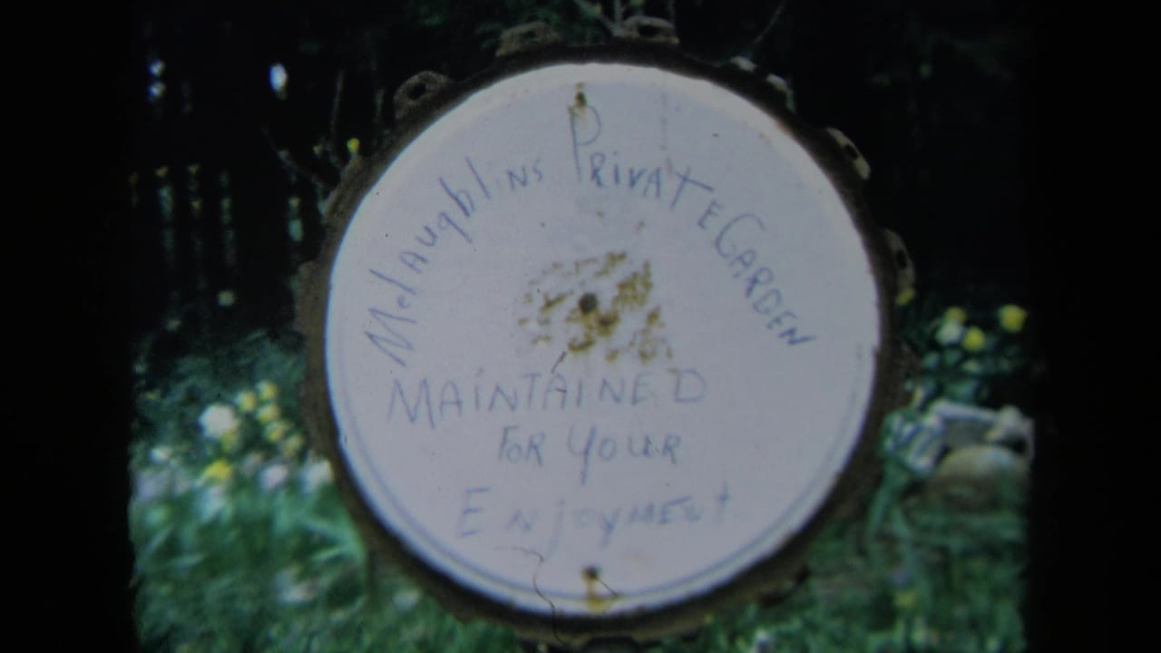 Round hand-painted private garden sign hanging among greenery.