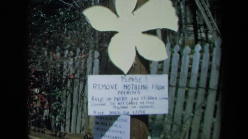 The final frame shows the posted visitor rules below the white flower sign, with fence slats and shrubs behind it.