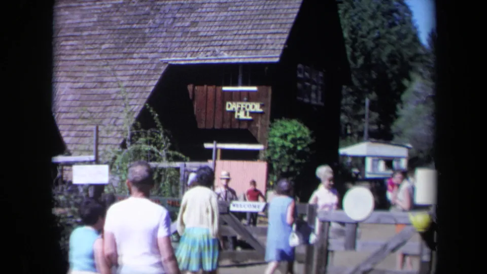 1969 California home-movie frame showing visitors near the wooden Daffodil Hill sign and entrance gate.