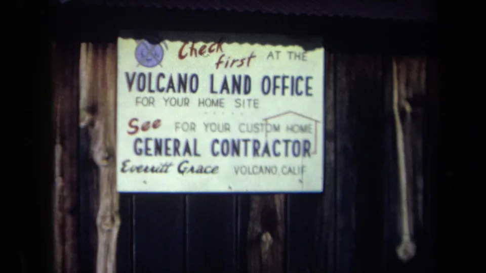 1969 California 8mm close-up of a Volcano Land Office sign advertising home sites and a general contractor.