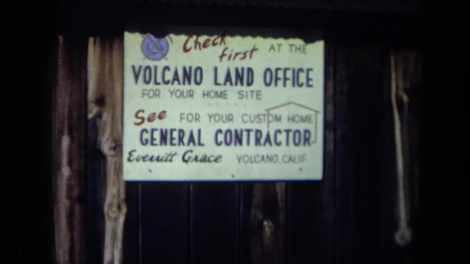 1969 California 8mm frame showing a Volcano Land Office sign advertising home sites and a general contractor.