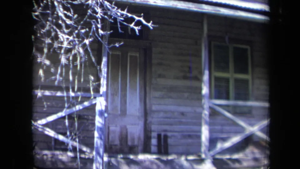 1969 California 8mm frame showing the house porch more closely, with a closed door, window, cross railings, and bright bare branches.