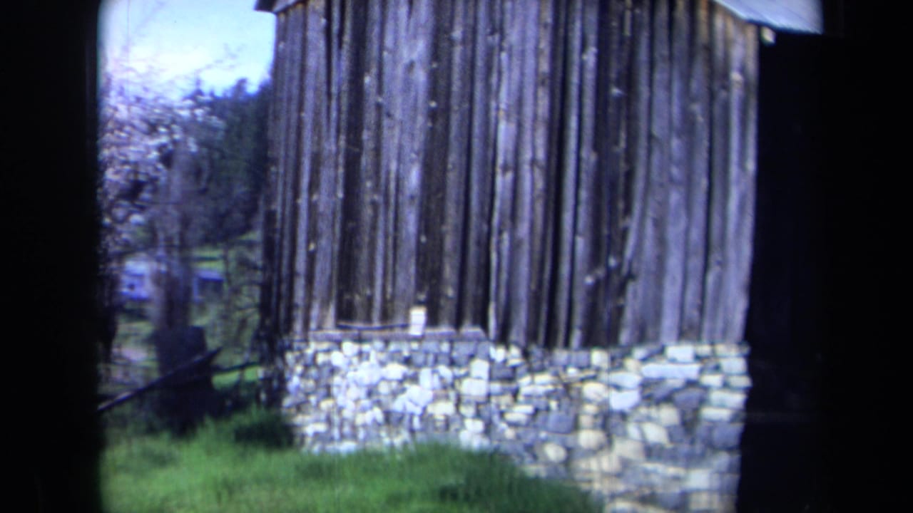 1969 California 8mm frame showing a rustic wooden building with a stone foundation, grass, trees, and dark film-edge framing.
