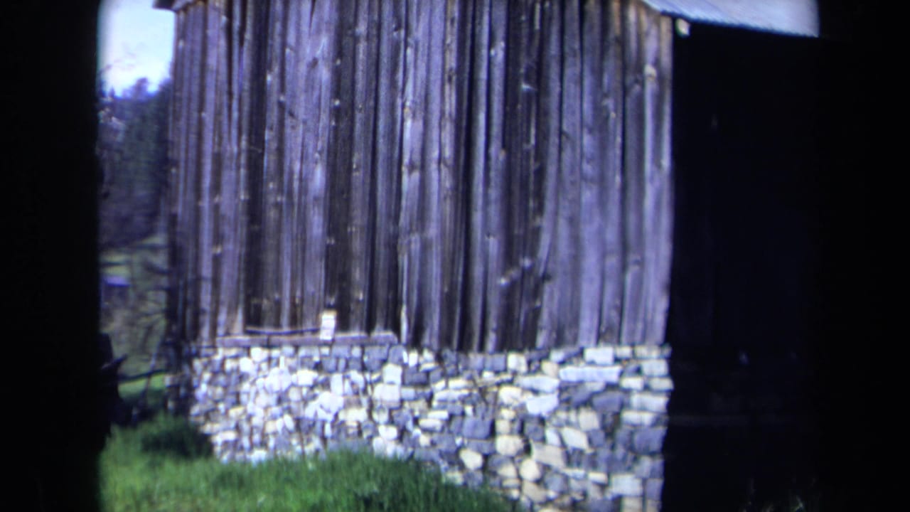 Wooden building and stone foundation seen from a similar angle with grass in front.