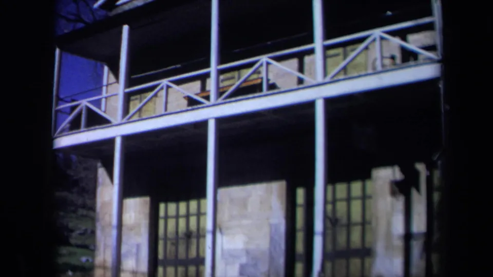 1969 California 8mm frame showing a historic hall exterior with stone facade, upper balcony, white posts, and dark film borders.