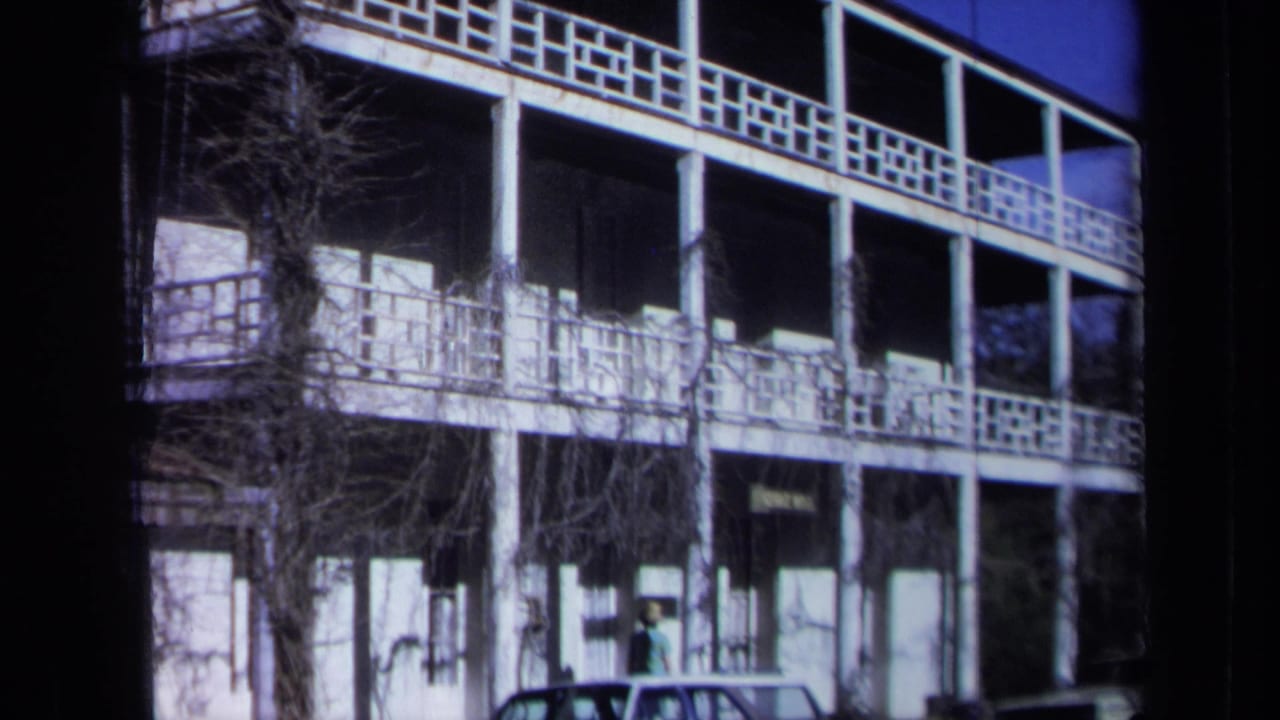 White multi-story inn facade with columns, balcony railings, vines, and a parked car below.