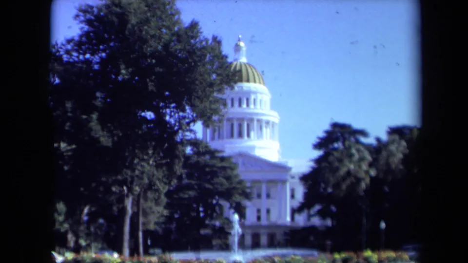 1969 8mm view of the California State Capitol in Sacramento, framed by trees with a fountain in the foreground.