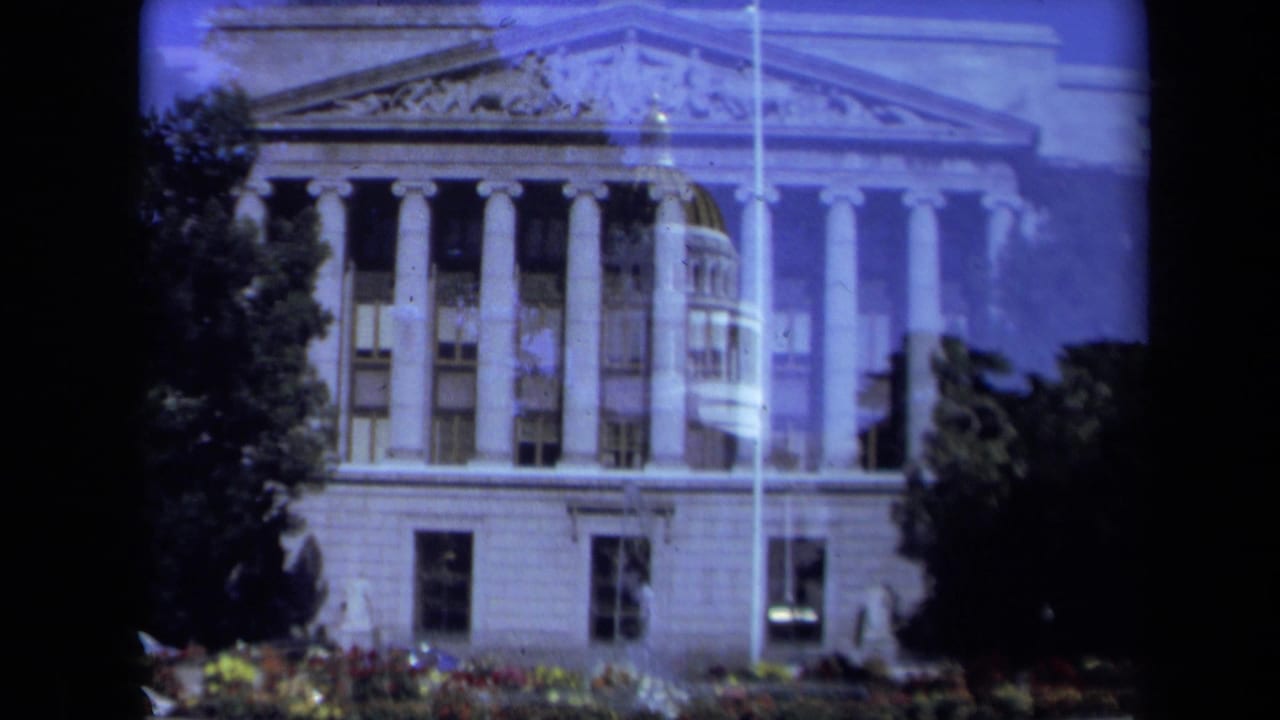 1969 California 8mm frame of a monumental public building facade with columns, pediment detail, trees, and flower beds.