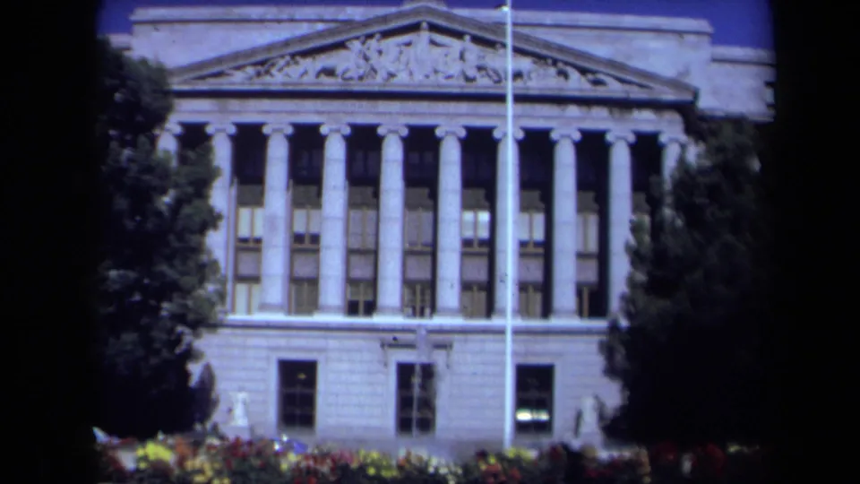 Closer 1969 California 8mm frame of the public building's columns, pediment, lower windows, flagpole, and landscaped beds.