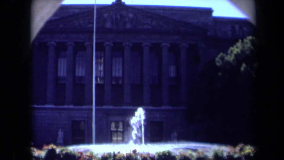 1969 California 8mm frame showing the columned landmark in shadow with a bright fountain spray and trees nearby.