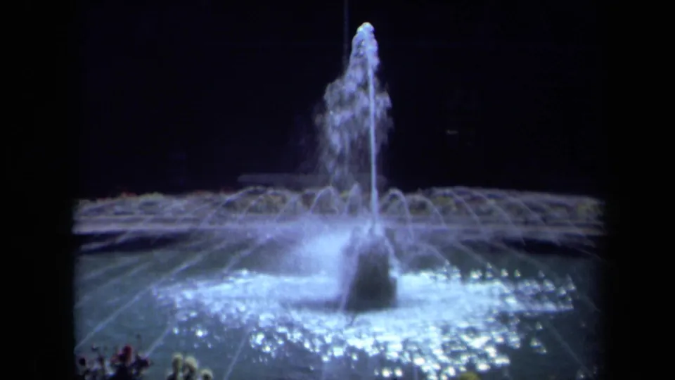 1969 California 8mm frame showing the fountain pool, central jet, and radiating illuminated spray in a nighttime setting.