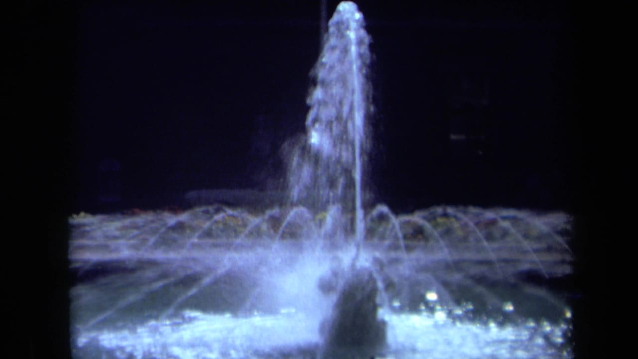 1969 California 8mm frame showing a lit fountain at night, with a tall central water jet and lower arcs spreading across the basin.