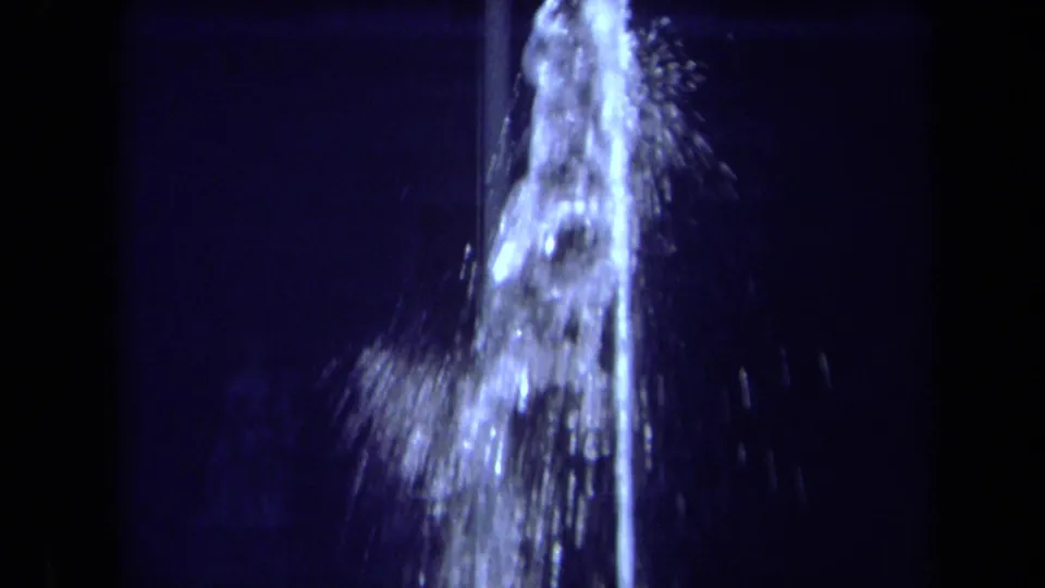 Tight 1969 California 8mm frame of the fountain spout and cascading spray, lit blue-white against the night.