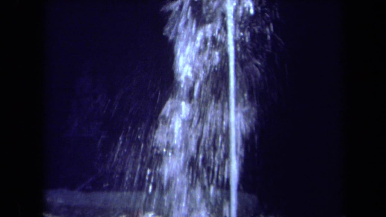 1969 California 8mm frame showing a tall illuminated fountain jet and misty spray at night.