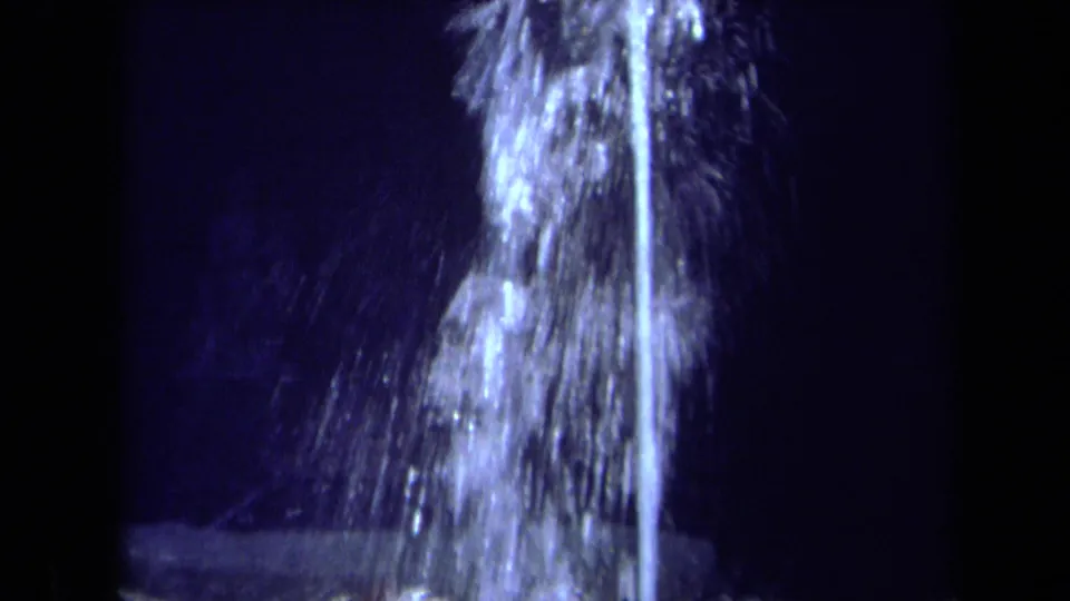 1969 California 8mm frame showing a tall illuminated fountain jet and misty spray at night.