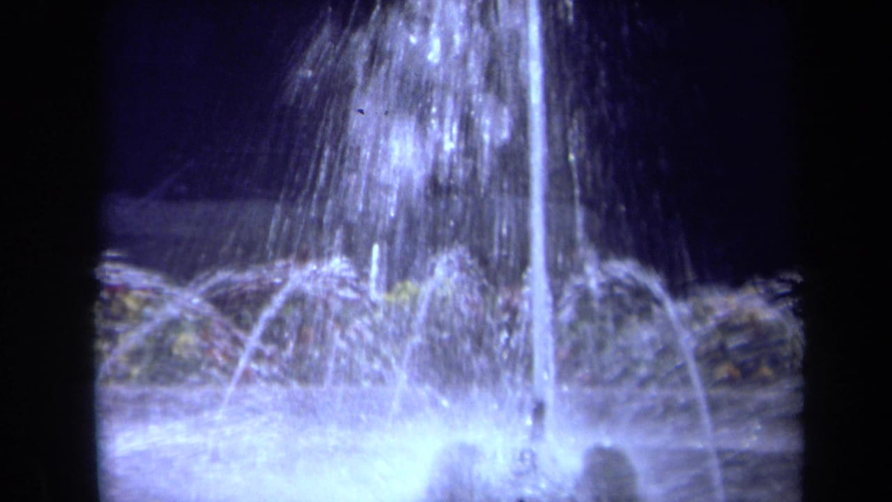 Illuminated fountain jets arc over a bright foamy basin at night.