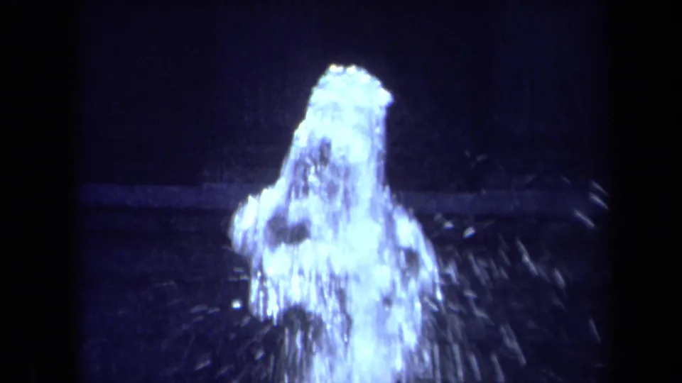 Close 8mm frame of the fountain's water jet in a California city park, with bright spray standing out against a dark shadowed backdrop.