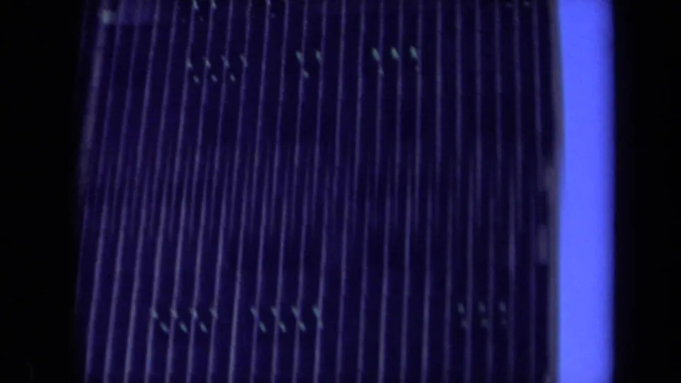 1969 California home-movie frame showing a closer section of the high-rise facade, with vertical ribs, dim windows, and blue twilight spill.