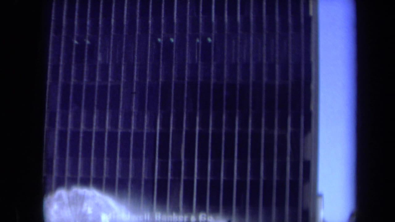 1969 California 8mm frame showing a dark office facade and partial Coldwell, Banker & Co. signage behind a misting fountain.
