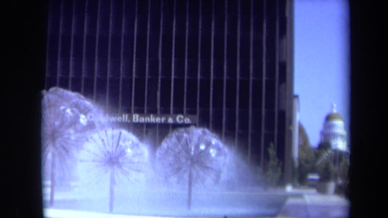 Spherical water fountains spray in front of a dark office building with a dome in the distance.