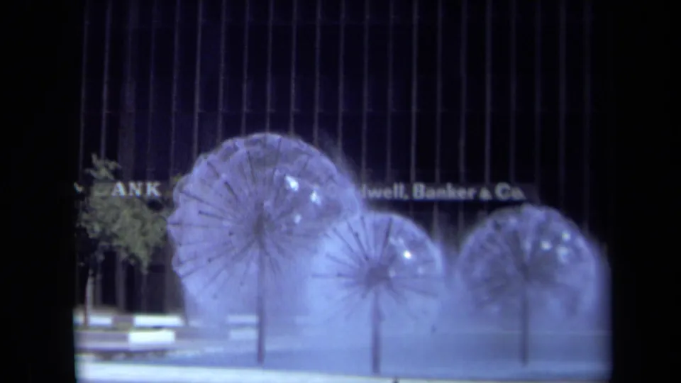 1969 California city frame showing three dandelion-like water fountains and Coldwell, Banker & Co. signage on a dark facade.