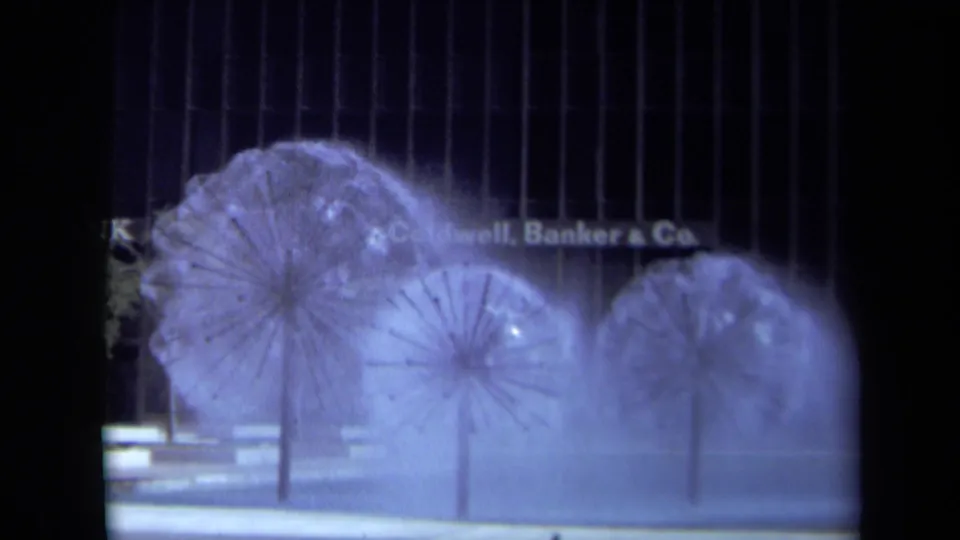 1969 California 8mm frame with misting sculptural fountains partly obscuring a modern office frontage and Coldwell Banker & Co. lettering.