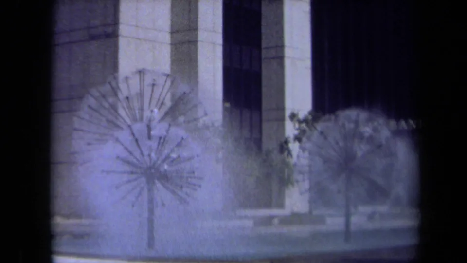 1969 California 8mm frame showing sculptural fountains beside a modern building entrance, with mist and architectural columns visible.