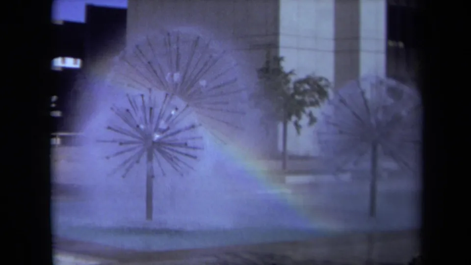 1969 Sacramento 8mm frame showing spiky metal fountains spraying mist in a public plaza as a rainbow appears across the water.