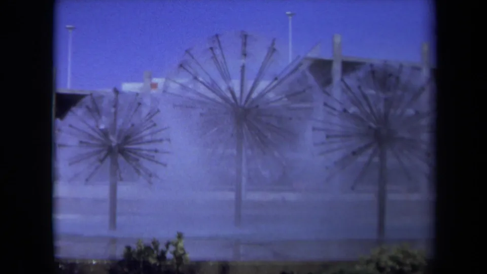 1969 Sacramento 8mm frame showing three dandelion-shaped fountains spraying water beneath a blue sky, with streetlights and buildings behind them.