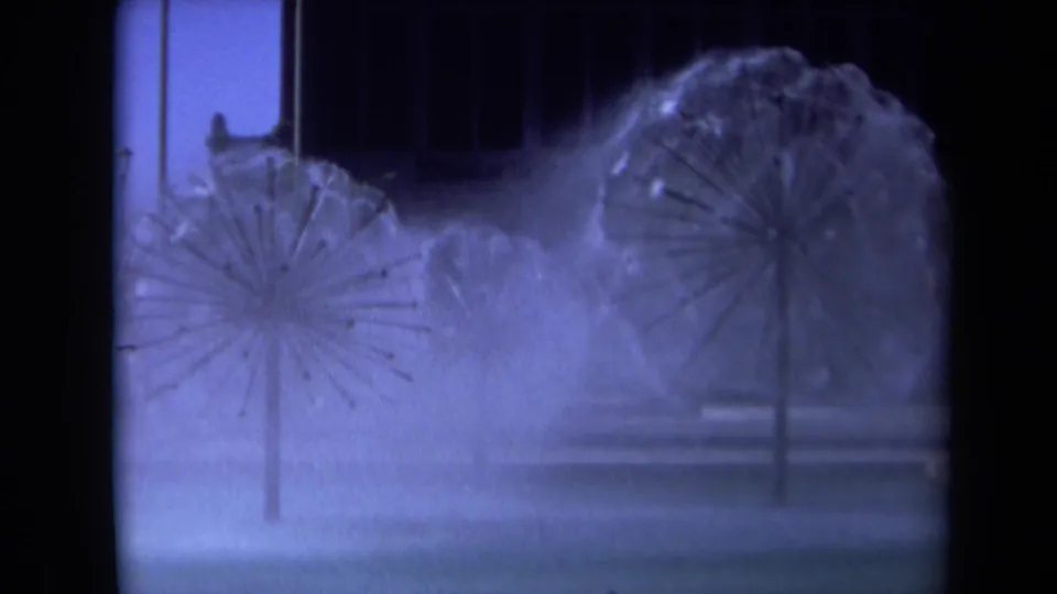 1969 Sacramento 8mm frame with starburst fountain sprays, hazy water mist, a dark building face, and tree shapes in the background.