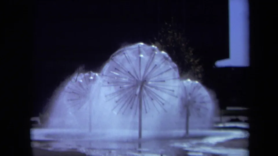 1969 Sacramento 8mm view of low, glowing dandelion sprinklers spreading water and mist across a night setting.
