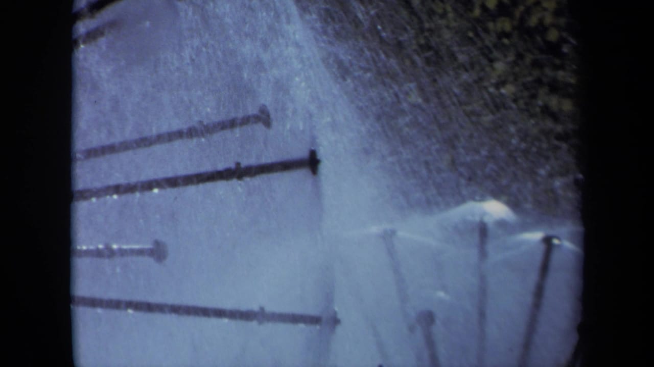 Cropped sprinkler arms spray across a pale blue field with dark film borders nearby.