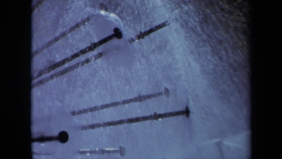 Close 8mm frame from the Sacramento sprinkler shot, showing overlapping metal arms and mist in a blue-tinted crop.