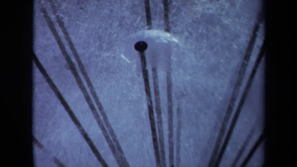 1969 Sacramento 8mm close-up of black sprinkler hardware, faint spray residue, and dark borders around a blue-tinted frame.