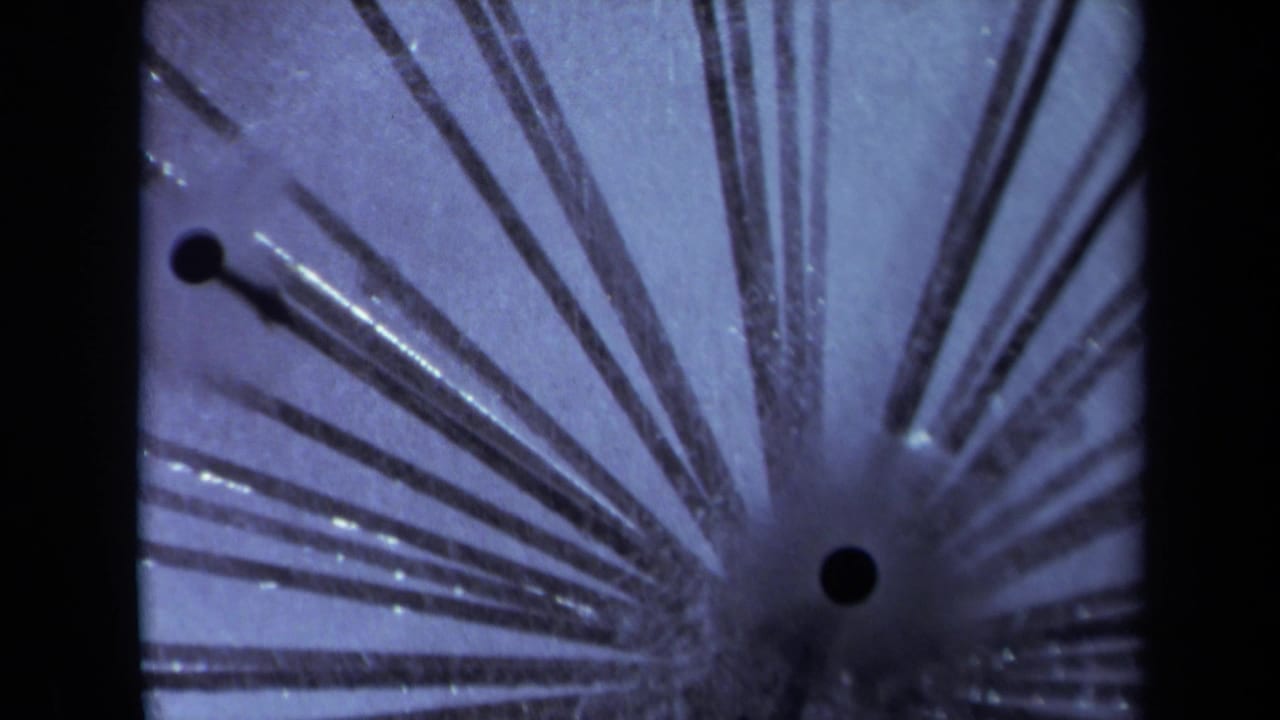 Close-up of radial conductive stems around a dark contact point on blue-purple 8mm film.