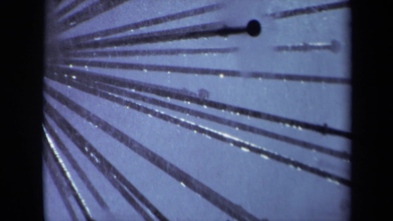 1969 Sacramento 8mm close-up of a metal sprinkler pattern, with dark radial tubes, fine water spray, and blue film tint.