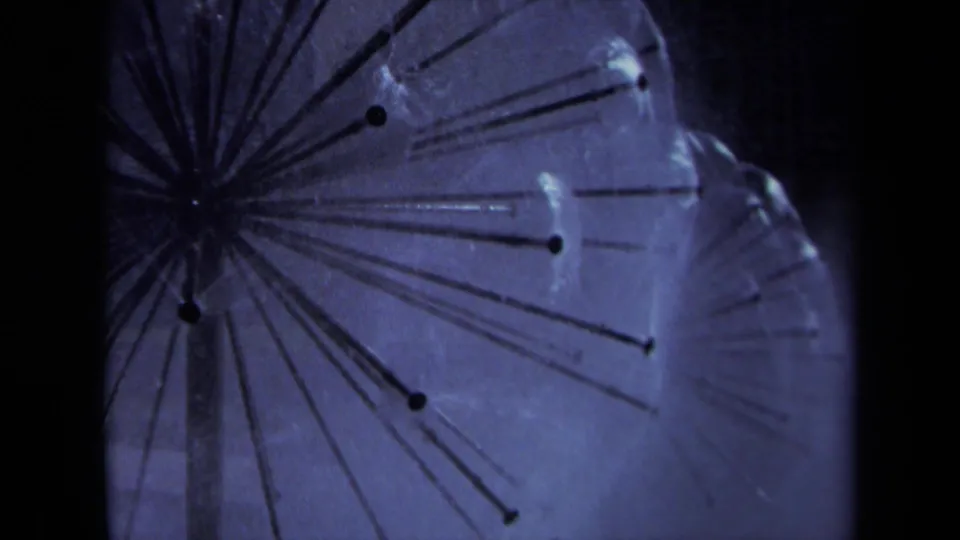1969 Sacramento 8mm close-up of a central sprinkler hub, with thin radiating tubes and water spray softened by grain and blue color shift.