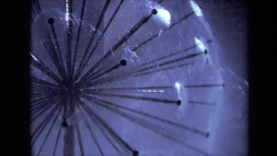 1969 Sacramento 8mm frame of a radial metal sprinkler head spraying water, with mist, dark tube ends, and visible black film borders.