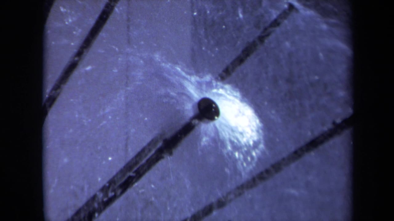 1969 Sacramento 8mm frame showing a sprinkler nozzle and bright water spray against a cool-toned pale background.