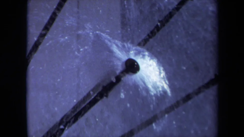 1969 Sacramento 8mm frame of a sprinkler head in motion, with water droplets catching light near dark diagonal lines.
