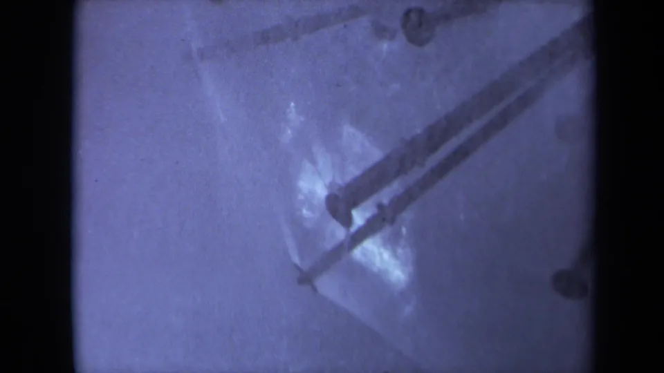 1969 Sacramento 8mm frame showing two dark metal strips across wet reflective material, with grain, blur, and visible gate edge.