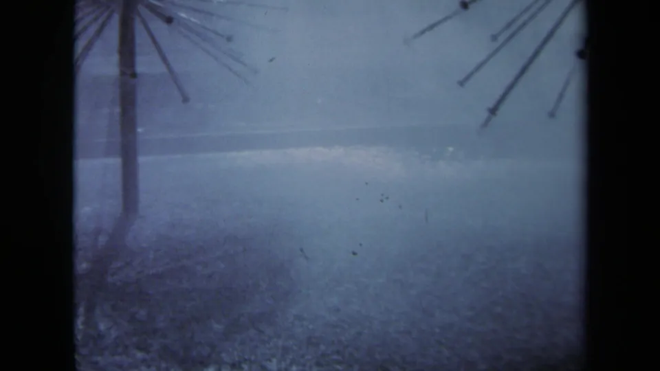 1969 Sacramento 8mm frame showing two metal supports and partial radiating structures above rain-slick pavement.