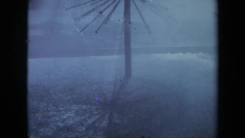 Blue-tinted 8mm frame from Sacramento in 1969 showing a spoked umbrella stand in heavy rain over wet ground.