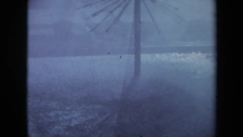 Final 1969 Sacramento 8mm frame showing the umbrella support fading into rain, pooled water, and dark gate-edge shadows.