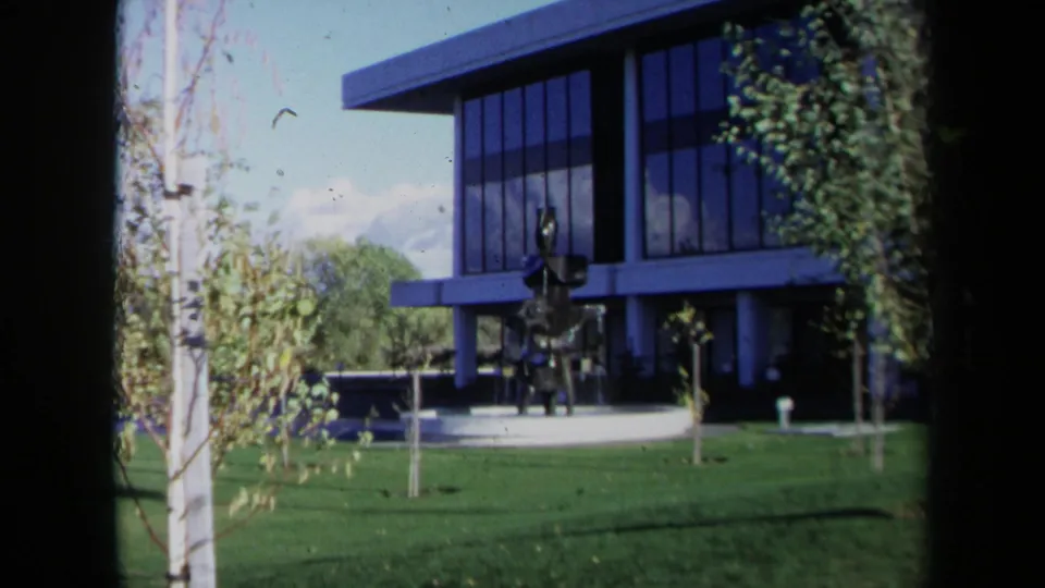 1969 Sacramento 8mm frame showing the modernist building exterior with sculpture, lawn, trees, and bright daylight.