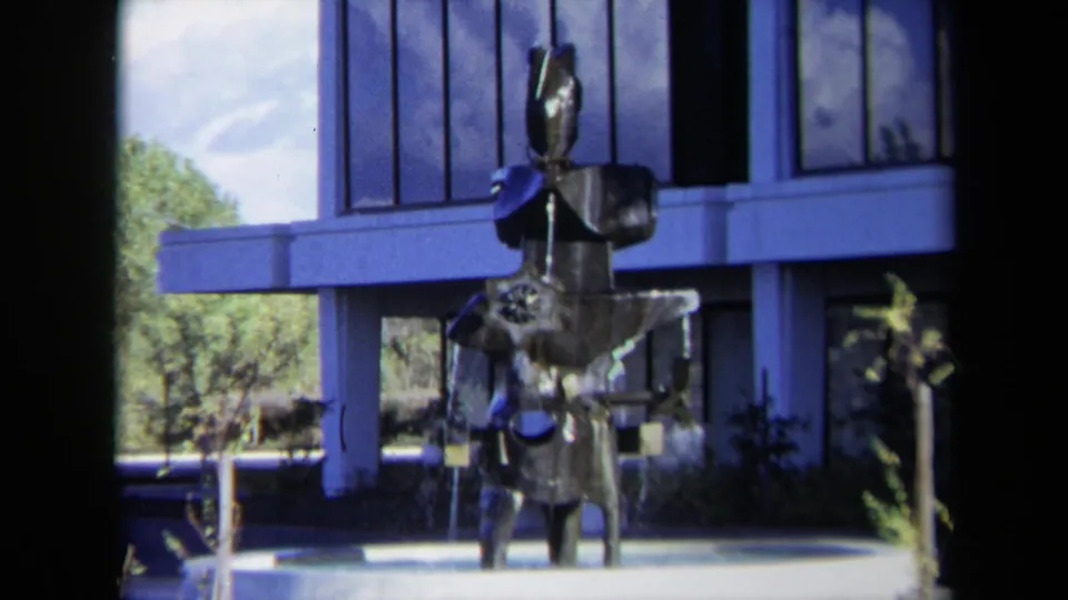 1969 Sacramento view of the metal fountain sculpture with gear-like forms, water spray, windows, and trees in the background.